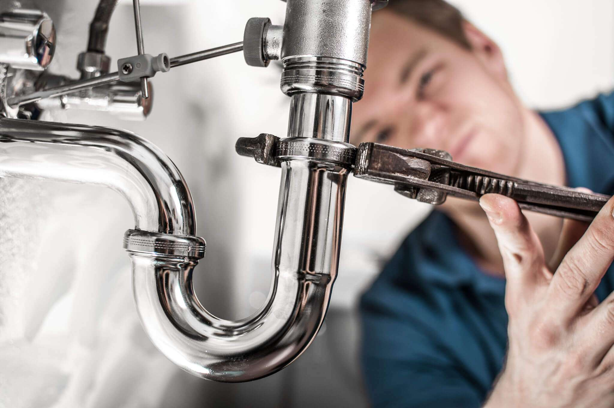 Plumber installing new chrome faucet under a bathroom sink